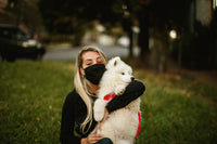 Femme blonde tenant son chien blanc dans ses bras.